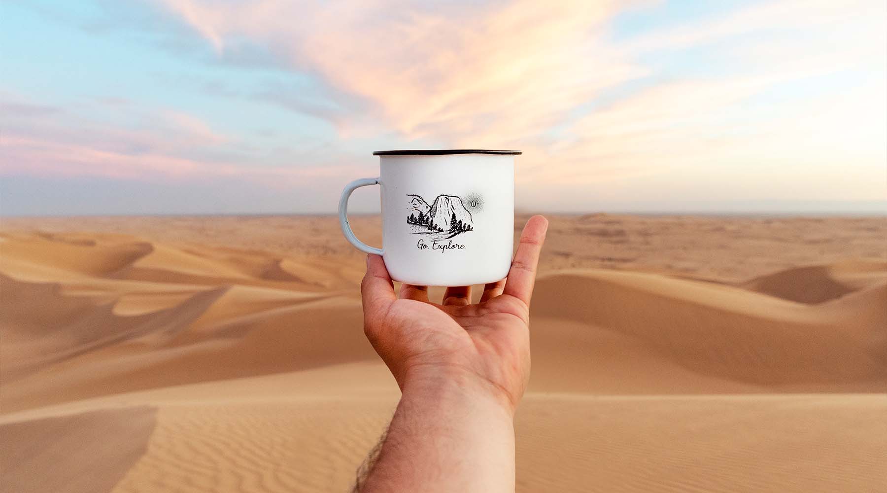 Glamis sand dunes desert with a seven seas roasting mug in the foreground with an hand holding it mid air.